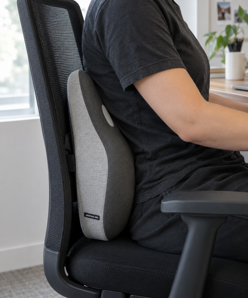 Person sitting at a desk with the OrthoCore lumbar support pillow behind their lower back on a mesh office chair