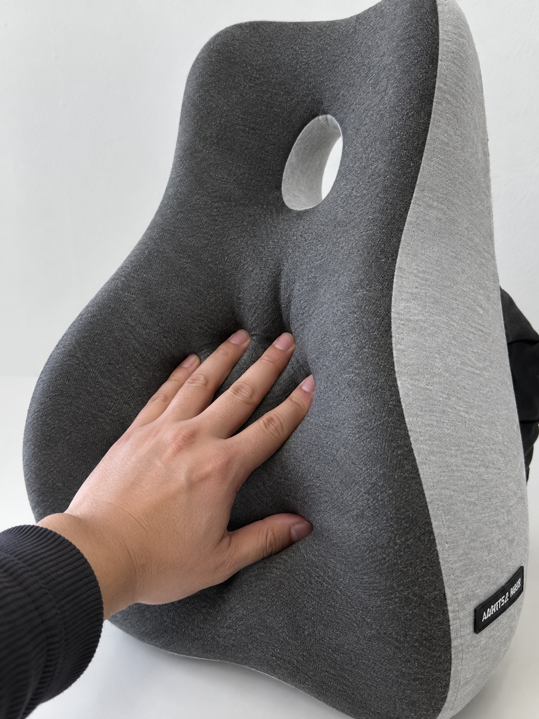 Hand pressing into the OrthoCore lumbar pillow showing the memory foam compress