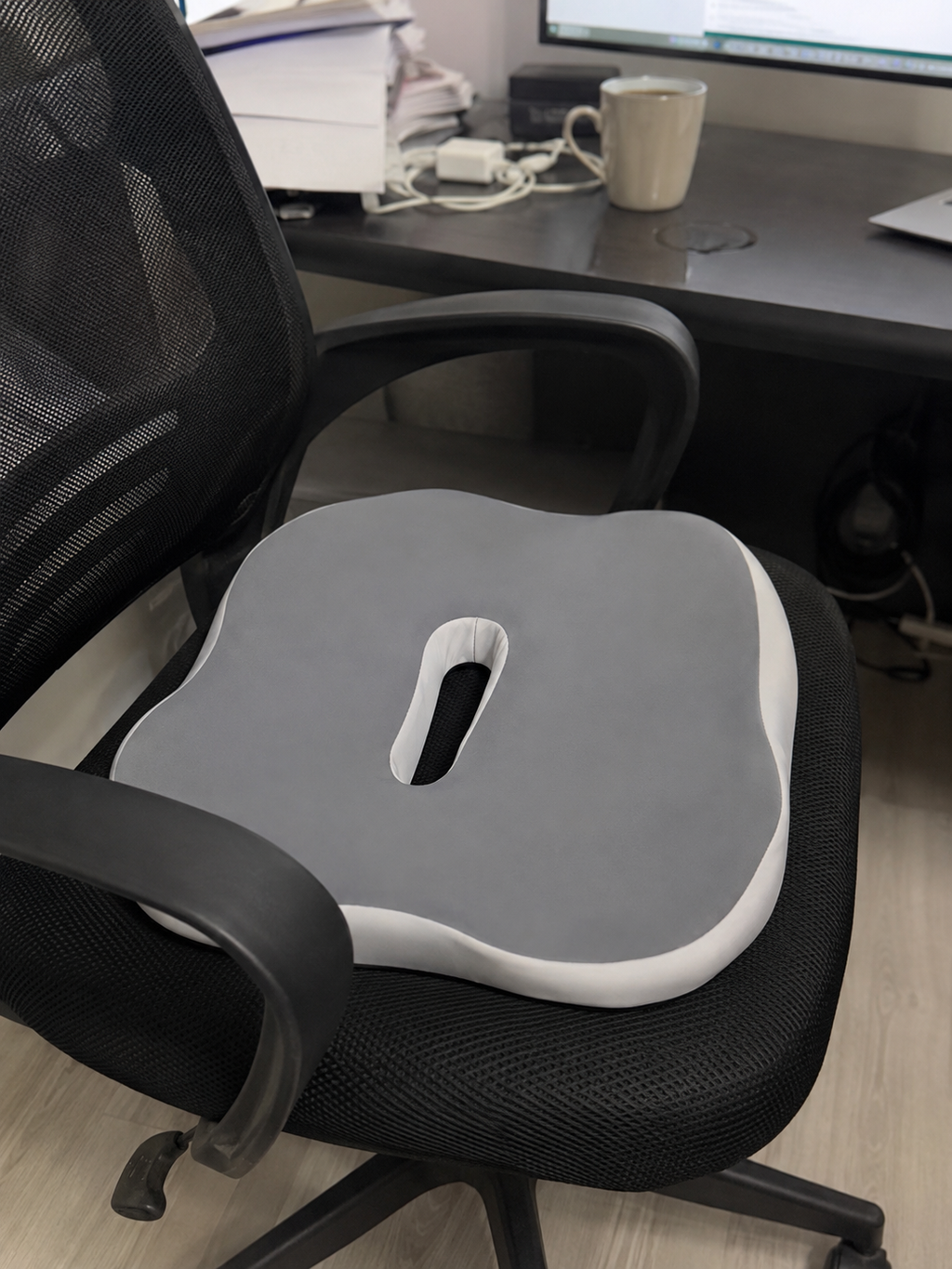 Grey OrthoCore memory foam seat cushion on a mesh office chair at a home office desk